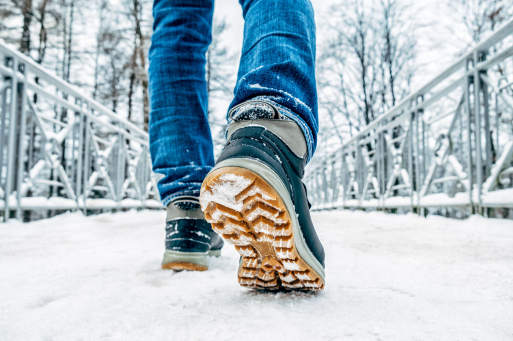 Un homme avec des jeans marche dans la neige avec une paire de botte au semelle orange et don la couleur est bleu et gris